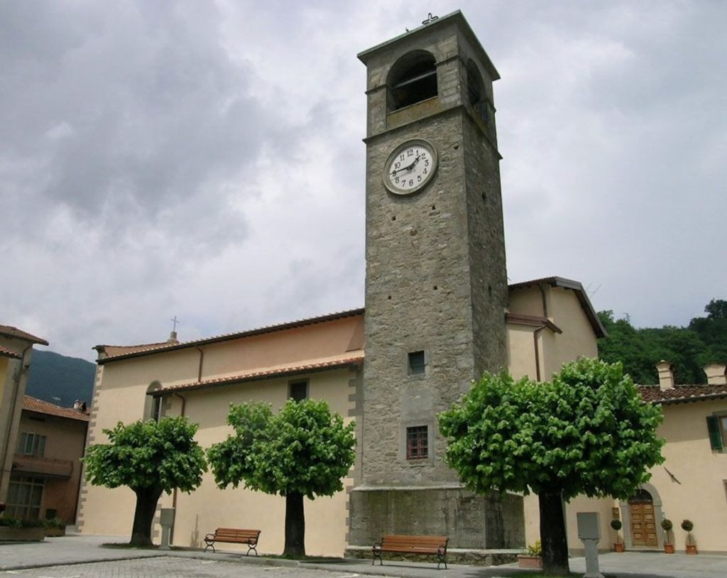 Il campanile in pietra e la facciata della chiesa visti dalla piazza, con i tigli in estate.